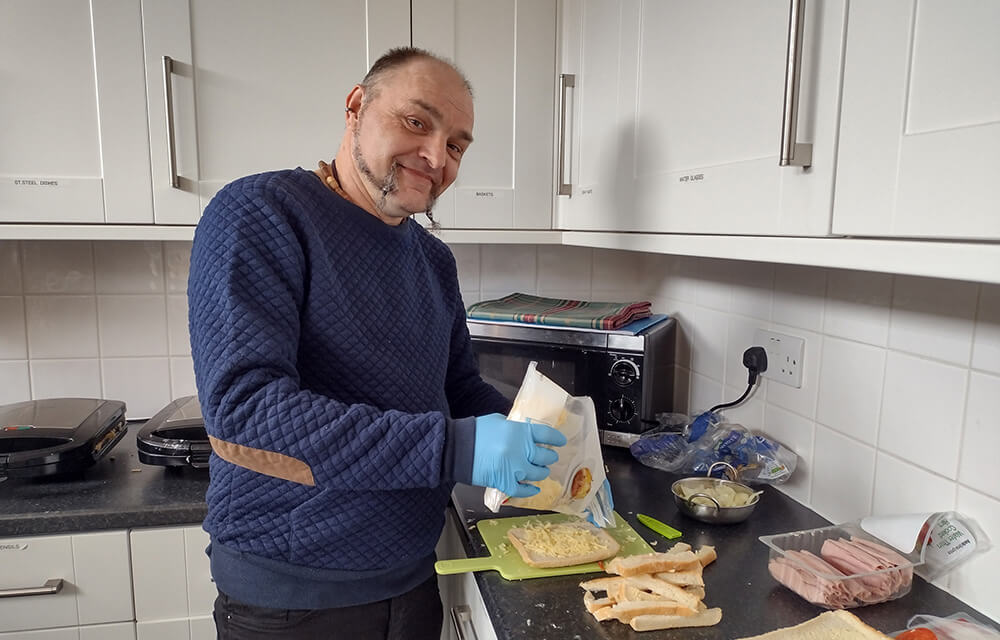 Man making cheese toastie and smiling at camera