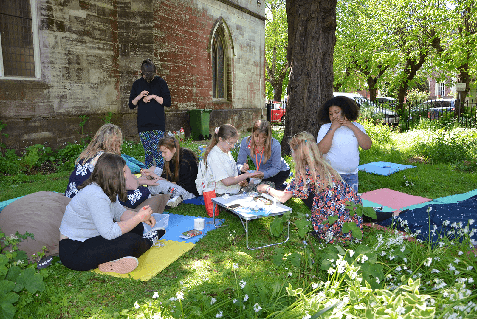 A group of teenagers and adults sitting on the grass and painting henna