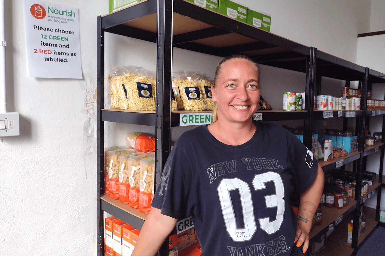 A smiling woman, stands in front of shelves of food