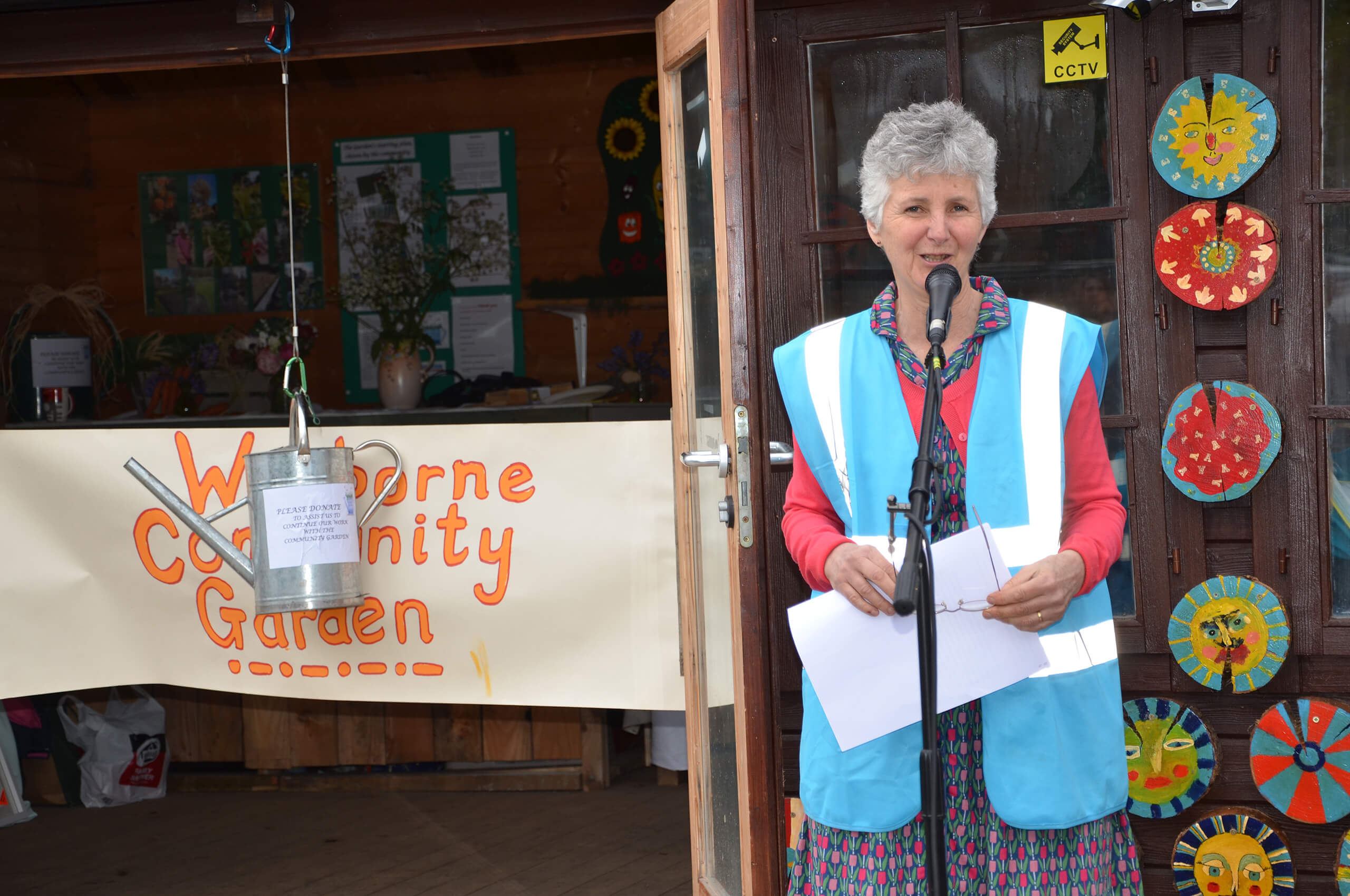 Woman stands at a microphone next to a shed