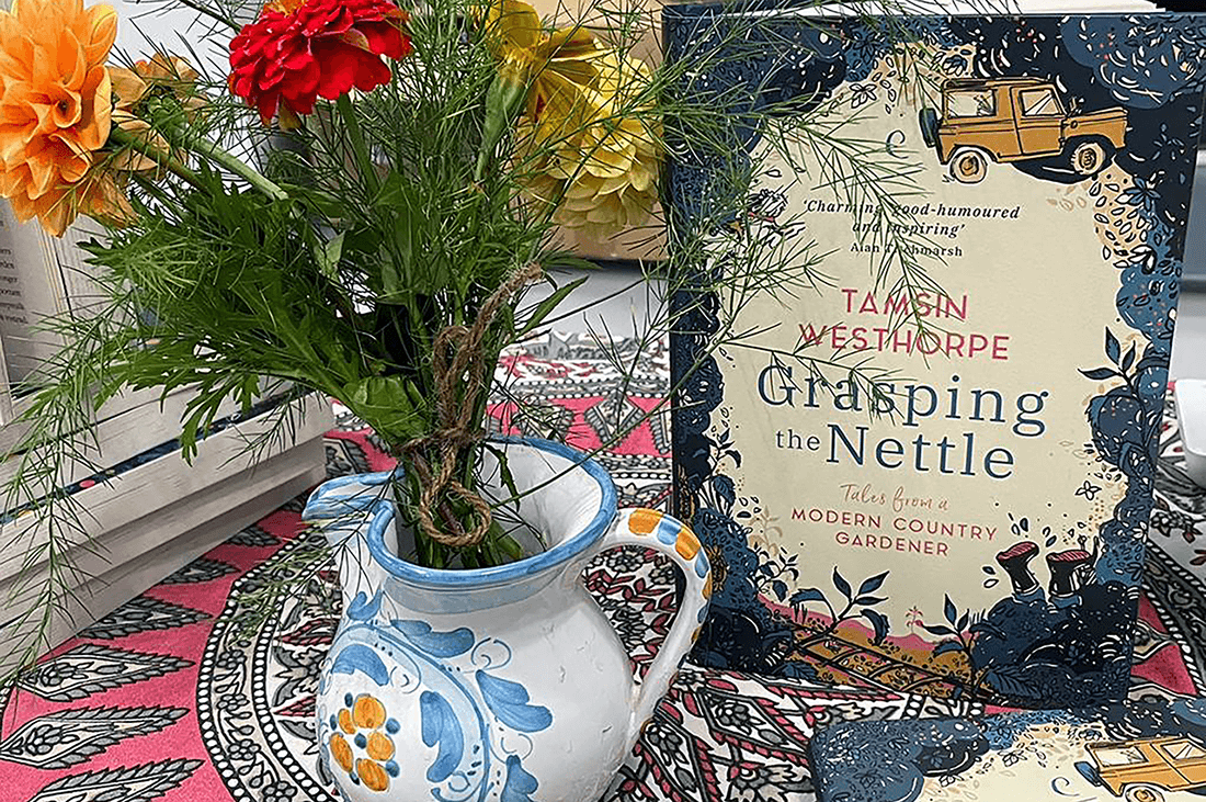 A jug with flowers stood nest to a book with the title "Grasping the Nettle" by Tamsin Westhorpe