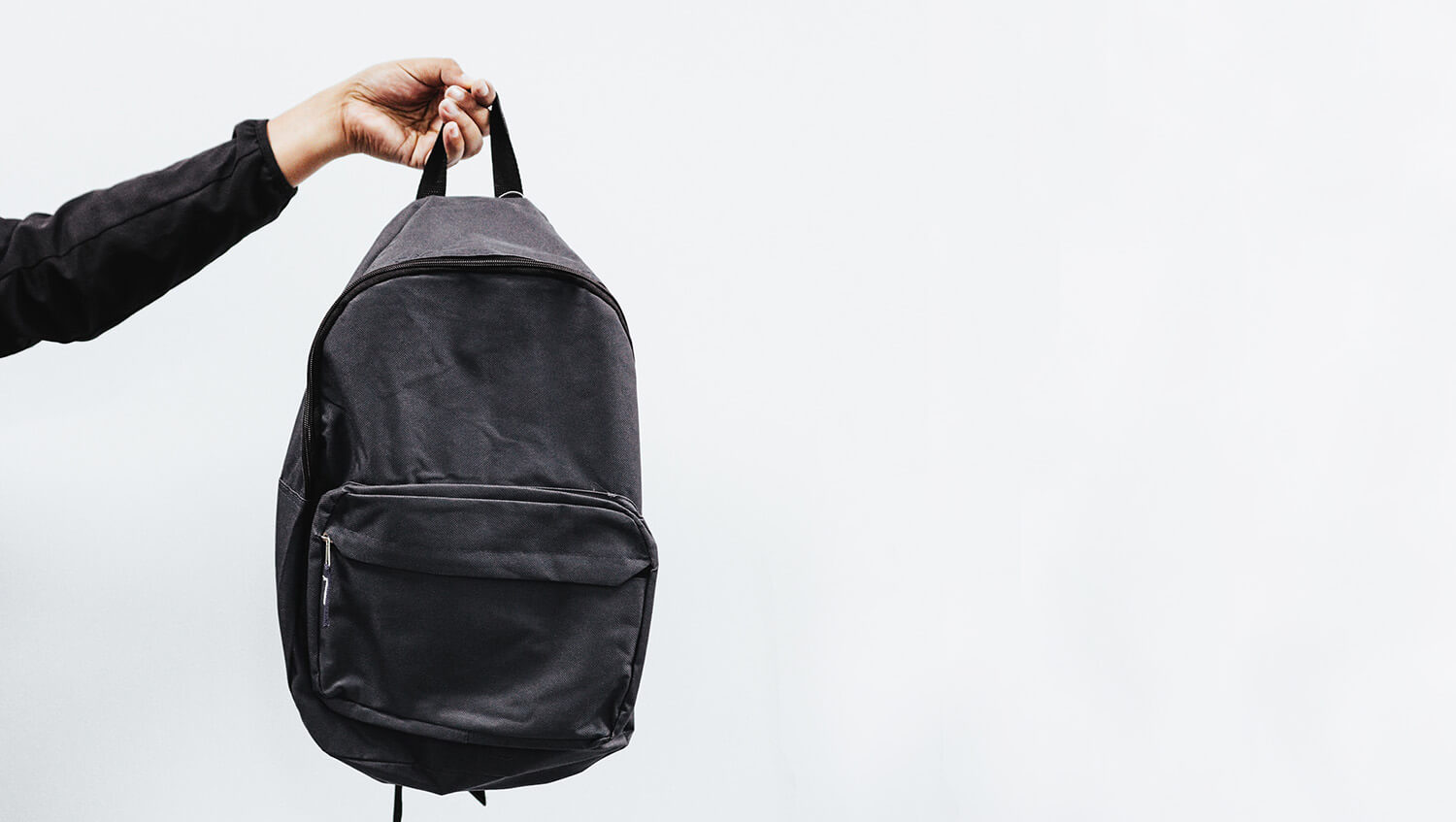 Arm holding a black rucksack against a white background