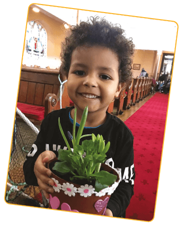 A child stands holding a pot plant and smiling at the camera