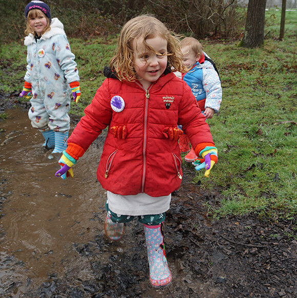 Two young smiling girls and a toddler walk through muddy puddles