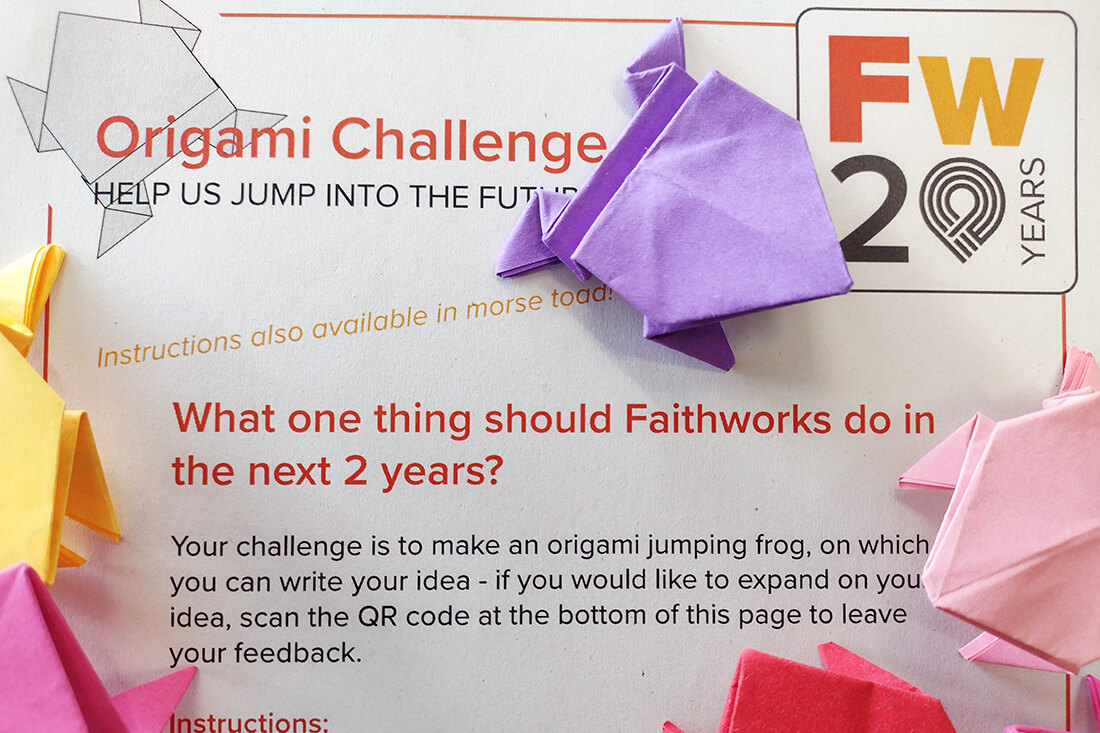 A sheet of paper with the words Origami Challenge written on. Origami frogs are scattered over the top.