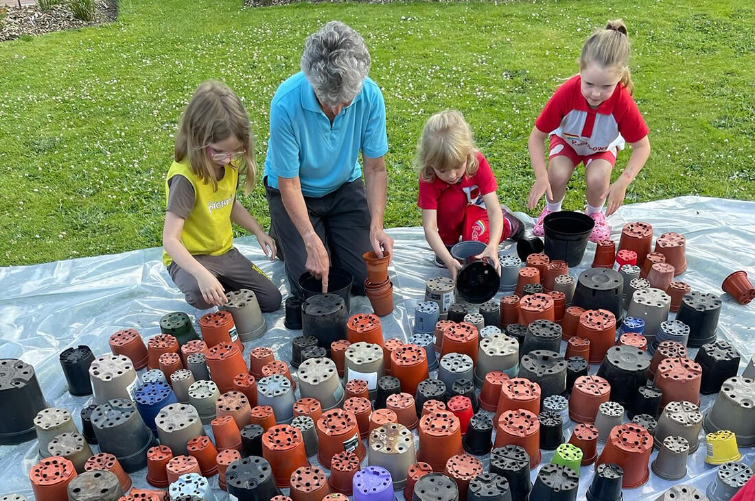 Three young girls help a woman with flower pots