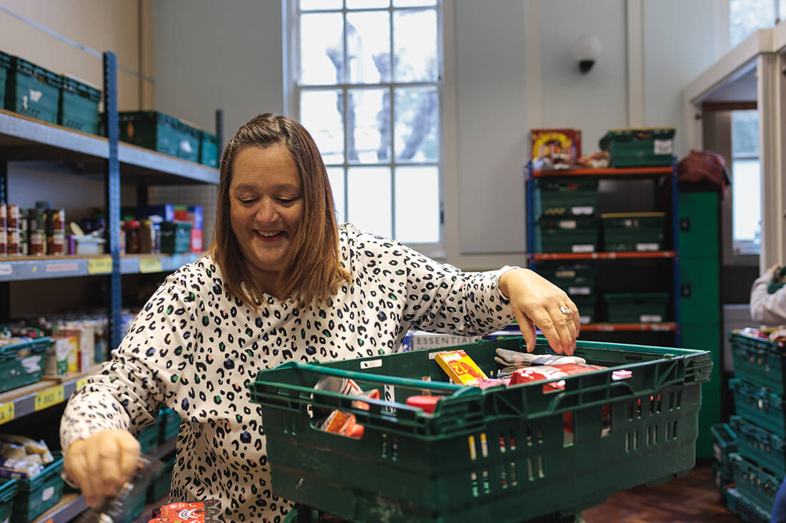 A smiling woman sorts through food items in a warehouse