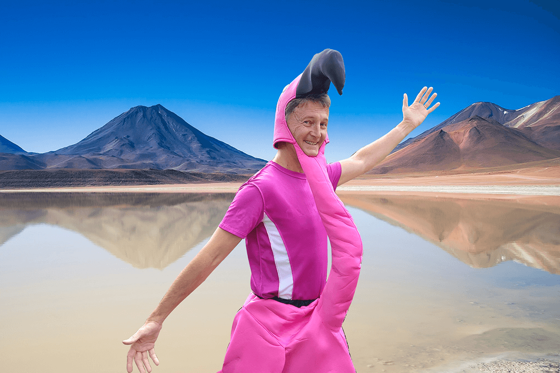 A man in a flamingo outfit, stands in front of salt flats, smiling and with his arms outstretched