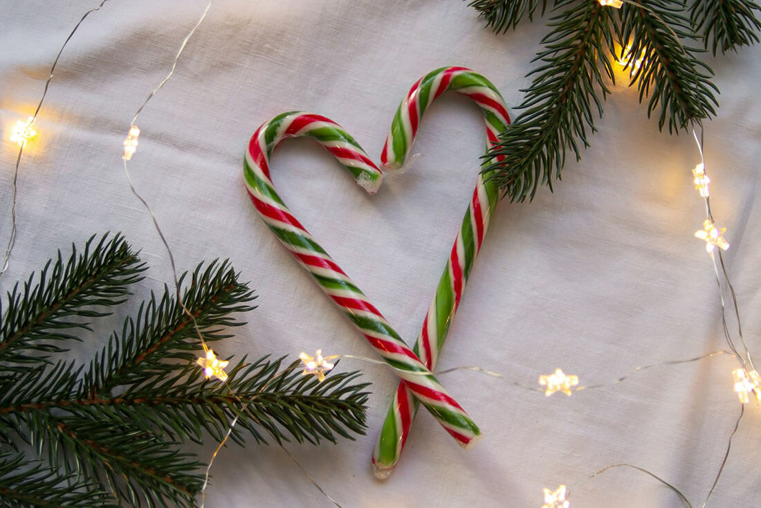 Candy canes in the shape of a heart, fir branches and star fairy lights on a table cloth