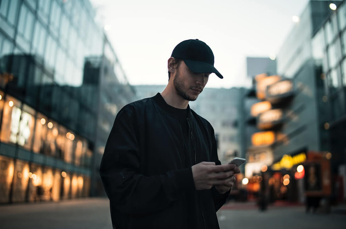 A man in a black jumper and cap looks at his mobile