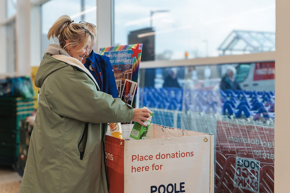 A smiling woman places food items into a large basket
